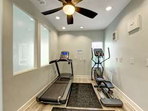 A treadmill and a stationary bike are in a room with a ceiling fan.