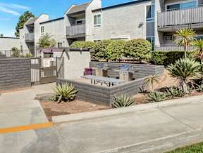 A concrete patio with a brick wall and a small garden in front of apartment buildings.