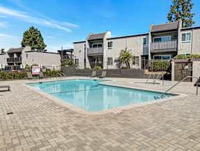 A swimming pool surrounded by a brick patio and apartment buildings.