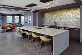A modern kitchen with a long white island and yellow chairs.