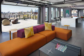 A modern living room with a large orange sofa and a glass table with a chess board on it.