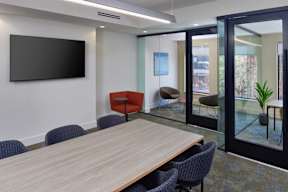 A conference room with a long table, chairs, and a television on the wall.