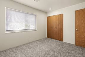A room with a window, carpeted floor, and two wooden doors.