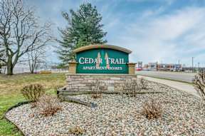 A sign for Cedar Trail Apartments is displayed in front of a gravel area.