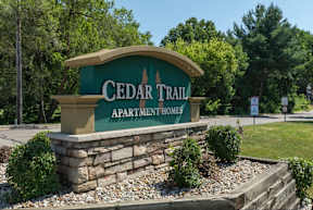 A sign for Cedar Trail Apartment Homes is displayed in front of a grassy area.