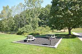 A picnic table is surrounded by a gravel area in a grassy yard.