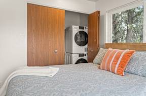 A bedroom with a bed, pillows, and a washing machine in the closet.