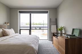 A bedroom with a bed, nightstand, and window overlooking a parking lot.