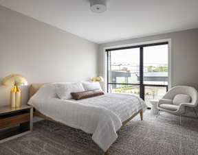 A bedroom with a large bed, a chair, and a window overlooking a balcony.