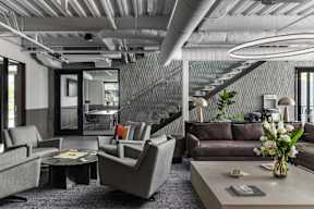 A modern living room with grey furniture and a glass staircase.