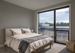 A bedroom with a large bed and a view of the outside through a sliding glass door.