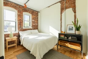 a bedroom with a bed and a dresser in front of a brick wall