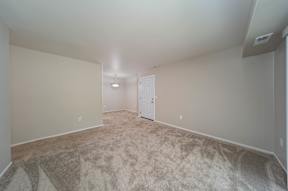 a spacious living room with carpet and a door to a bedroom