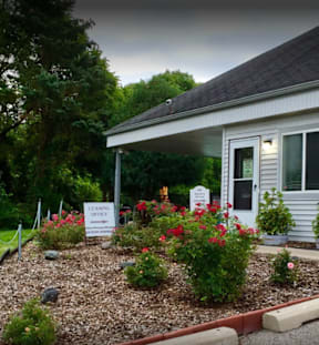 the front yard of a white house with flowers and a sign for a church
