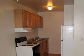 Galley style kitchen with cherry color cabinets, a white electric stove, and white fridge.