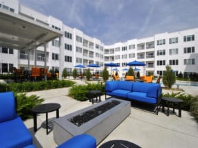 a patio with blue couches and chairs and umbrellas in front of an apartment building