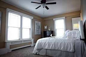 Primary bedroom with plush bed, carpeting, large windows, and a ceiling fan.
