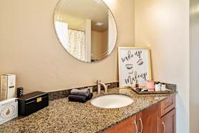A bathroom with a round mirror, sink, and a sign that says "wake up and makeup".
