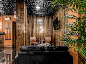 A black couch sits in front of a wooden wall with a TV mounted on it.