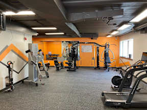 A gym with orange walls and a variety of exercise equipment.