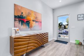A modern waiting room with a large abstract painting on the wall and a wooden bench.