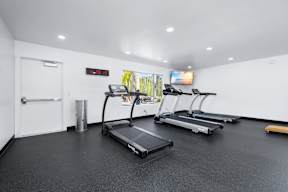 A gym with treadmills and a television on the wall.