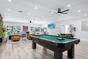 A pool table is in the middle of a room with a ceiling fan and a wall with pictures.