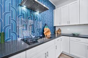 A kitchen with white cabinets and a blue patterned backsplash.