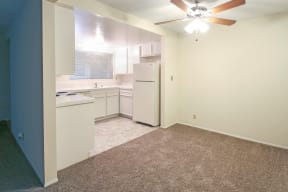 An empty kitchen with white appliances and a ceiling fan.