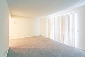 An empty living room with a large window with white blinds.