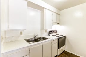 A small kitchen with white cabinets and a stove and sink.