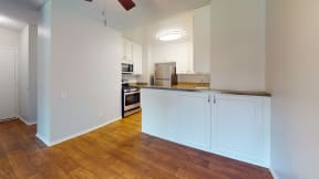 an empty kitchen with white cabinets and a wood floor at Charter Oaks Apartments, California, 91360