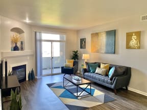 Windsor Denver Apartments - Interior View Of The Living Room Which Features Gold And Blue Artwork Hanging On The Wall, Large Glass Door That Leads Out To The Private Patio Space, Dark Navy Blue Sofa W