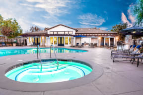 Pool with Lounge Chairs, Tables with Chairs, Umbrellas, Spa, and View of Clubhouse in the Background at Barrington Place, California