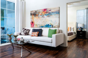 Living Room with Wood-Style Flooring, White Couch, Glass-Top Coffee Table, Wall Art, and Large Window at Barrington Place, Rancho Cucamonga, CA