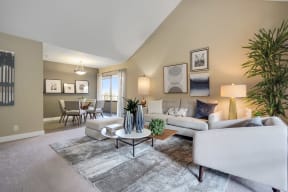 Mountain View, CA Apartments - Americana Apartments - Open-Floor Living Room With Carpet Flooring, High Ceiling, A Window With Blinds, A Modern Light Fixture, And A Dining Area