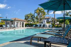 A pool with sun loungers and umbrellas is surrounded by trees at Missions at Chino Hills Apartments, California, 91709