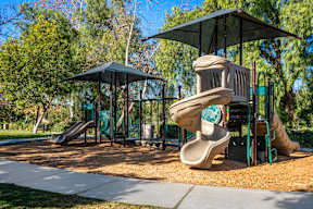Apartments Chino Hills, CA - Missions at Chino Hills - Playground Featuring Slides, Climbing Structures, and Canopy, Surrounded by Tress and Landscaped Grounds