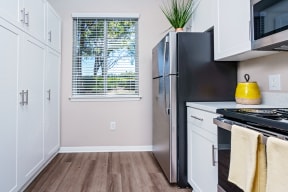 Apartments for Rent in Chino Hills - Missions at Chino Hills - Bright Kitchen With White Cabinets, Stainless Refrigerator, Electric Range, Wood Look Flooring, And Window With Blinds.