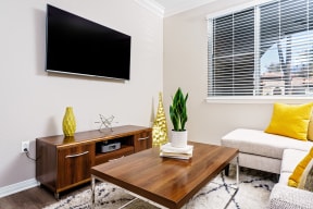 Dog-Friendly Apartments in Chino Hills, CA - Missions at Chino Hills - Living Room With Mounted Television, Wood Coffee Table, Media Console, Yellow Accent Pillows, And Large Window With Blinds.