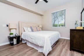 Two-Bedroom Apartments in Chino Hills, CA - Missions at Chino Hills - Spacious Bedroom With Upholstered Bed, Ceiling Fan, Nightstands With Lamps, Wood Style Flooring, And Window With Blinds.