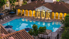 A pool surrounded by a building with a red tile roof.