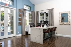 A room with a desk and chairs in front of a window with curtains.