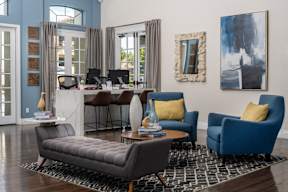 A living room with a grey sofa, a blue armchair, a coffee table, and a painting on the wall.