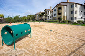 A playground with a green slide and sandy ground.