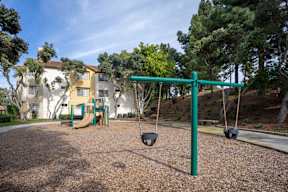 A playground with a green swing set and a building in the background.