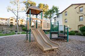 A playground with a slide and a green fence.