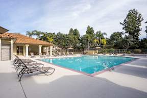 A large swimming pool with lounge chairs and a building in the background.
