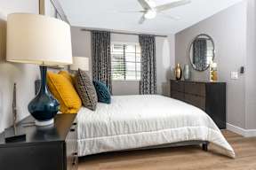 A bedroom with a white bed and a blue vase on a nightstand.
