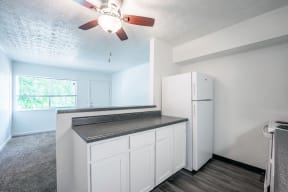 an empty kitchen with a refrigerator and a ceiling fan